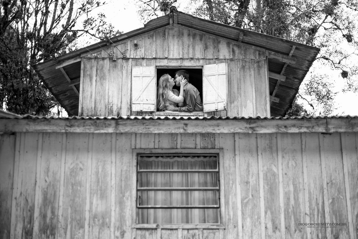 Casal se beijando em frente a uma janela. Foto tirada de fora.