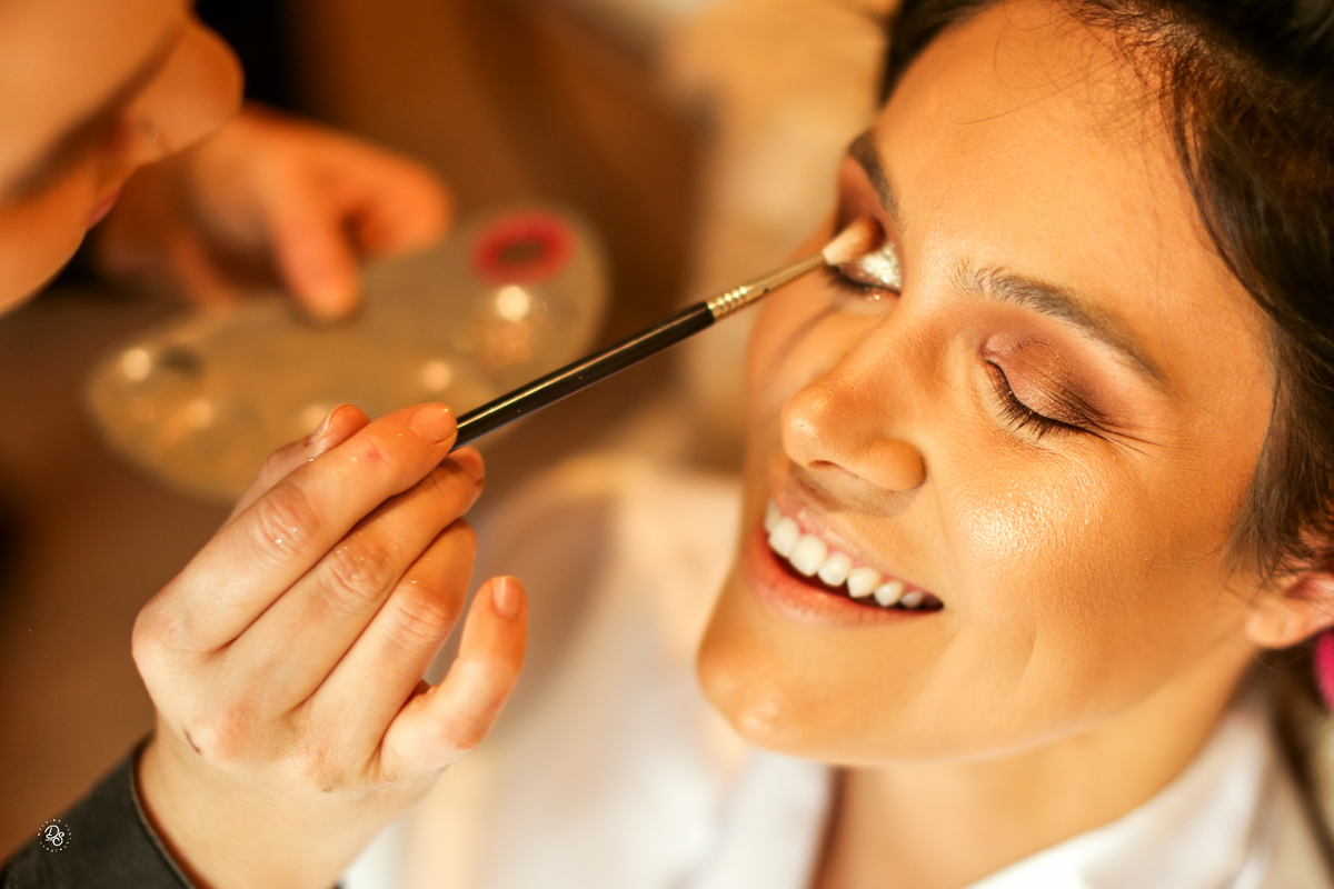 Noiva sorrindo ao ser maquiada.