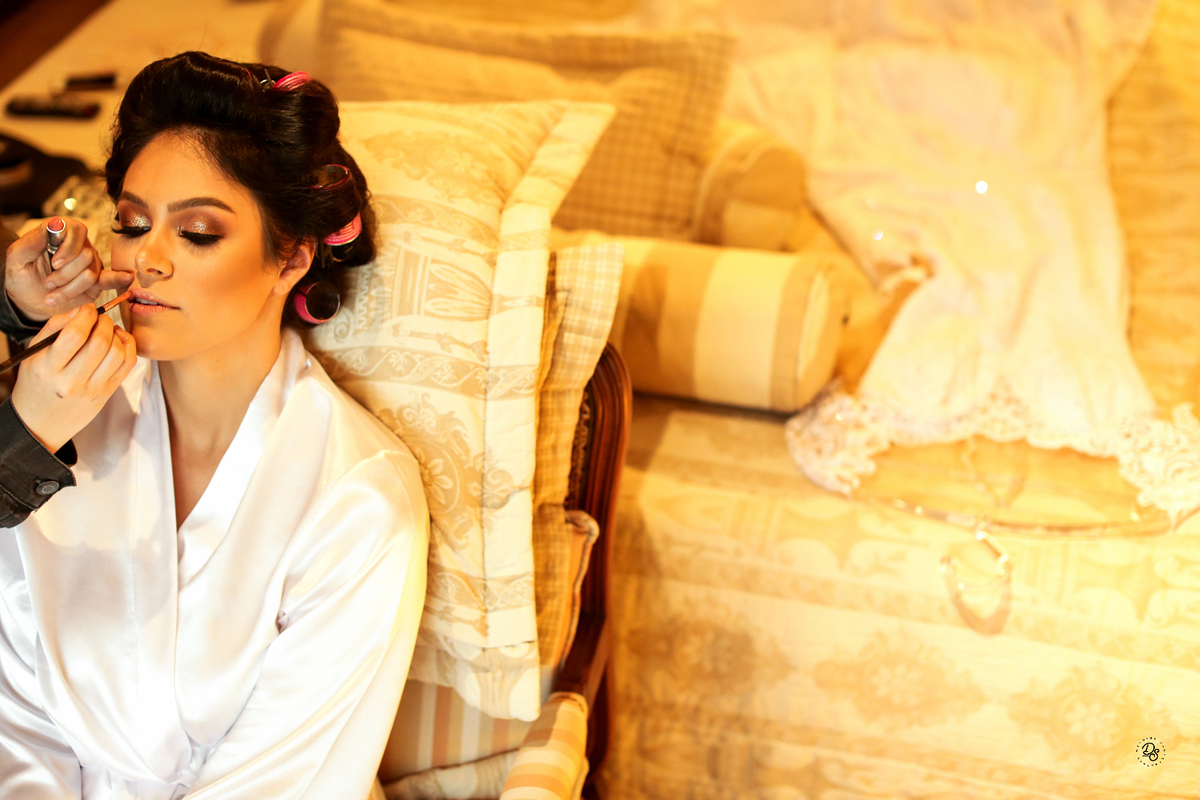 Detalhe da noite sendo maquiada com o seu vestido na cama.