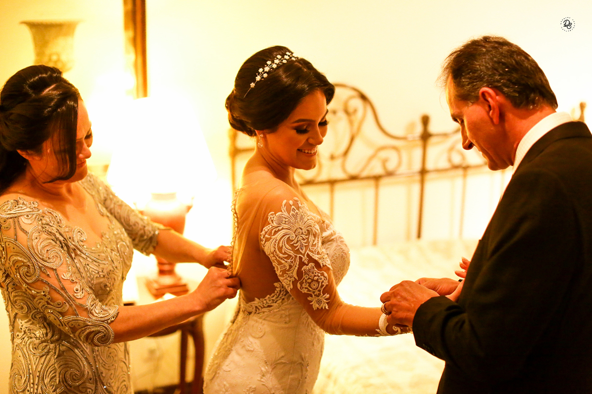 Mãe e pai ajudando a filha a se vestir para o grande dia.