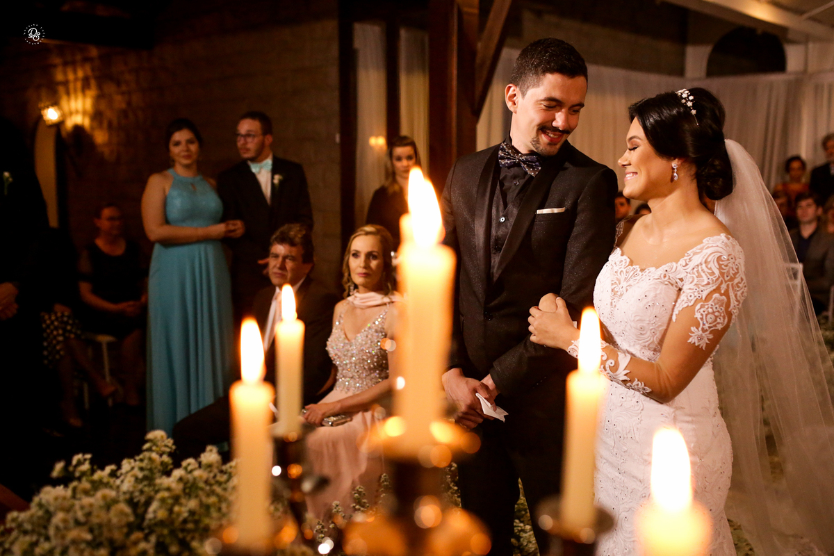 Noivos se olhando com velas desfocadas na imagem.