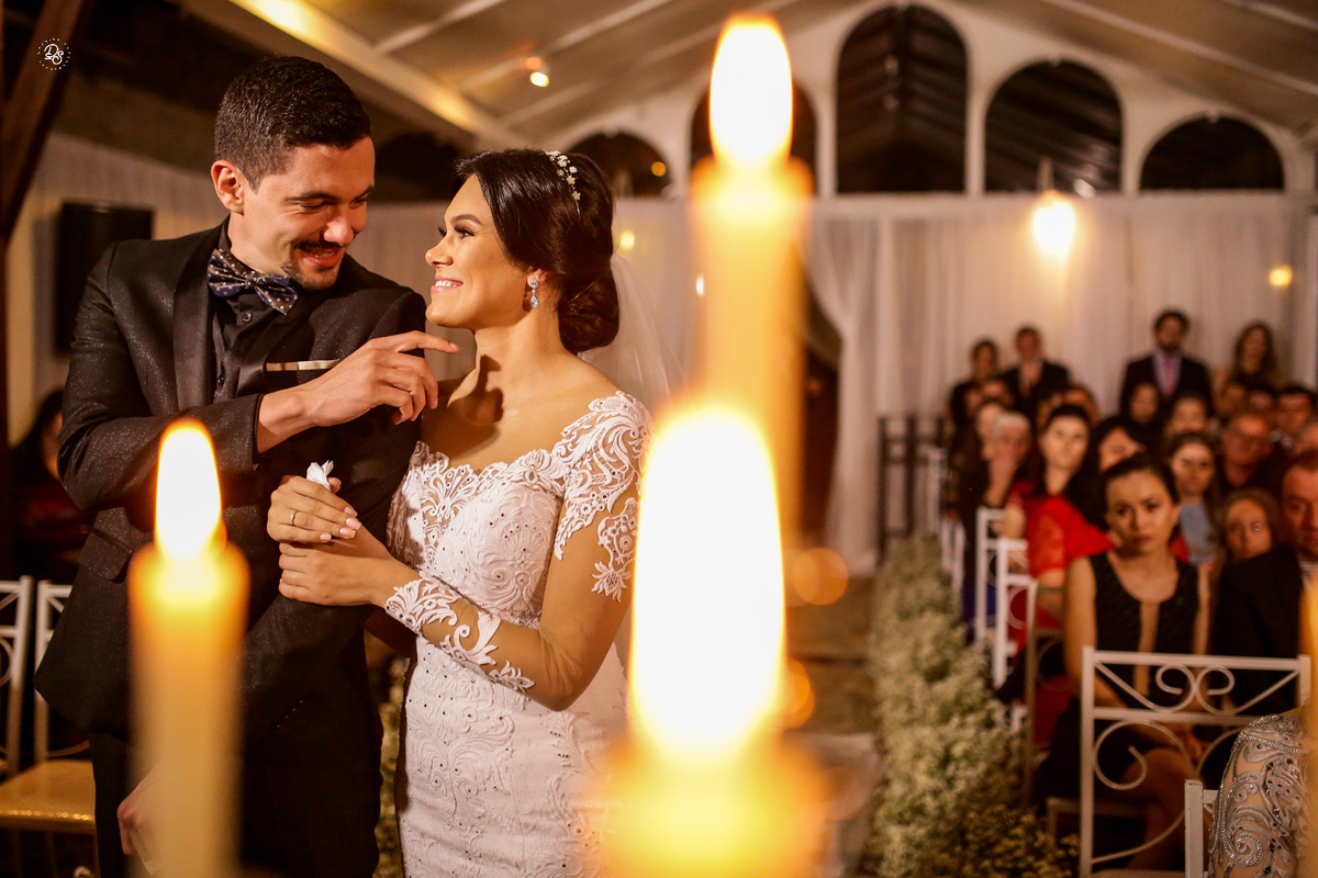 Noivos se olhando e sorrindo com detalhe das velas em desfoque.