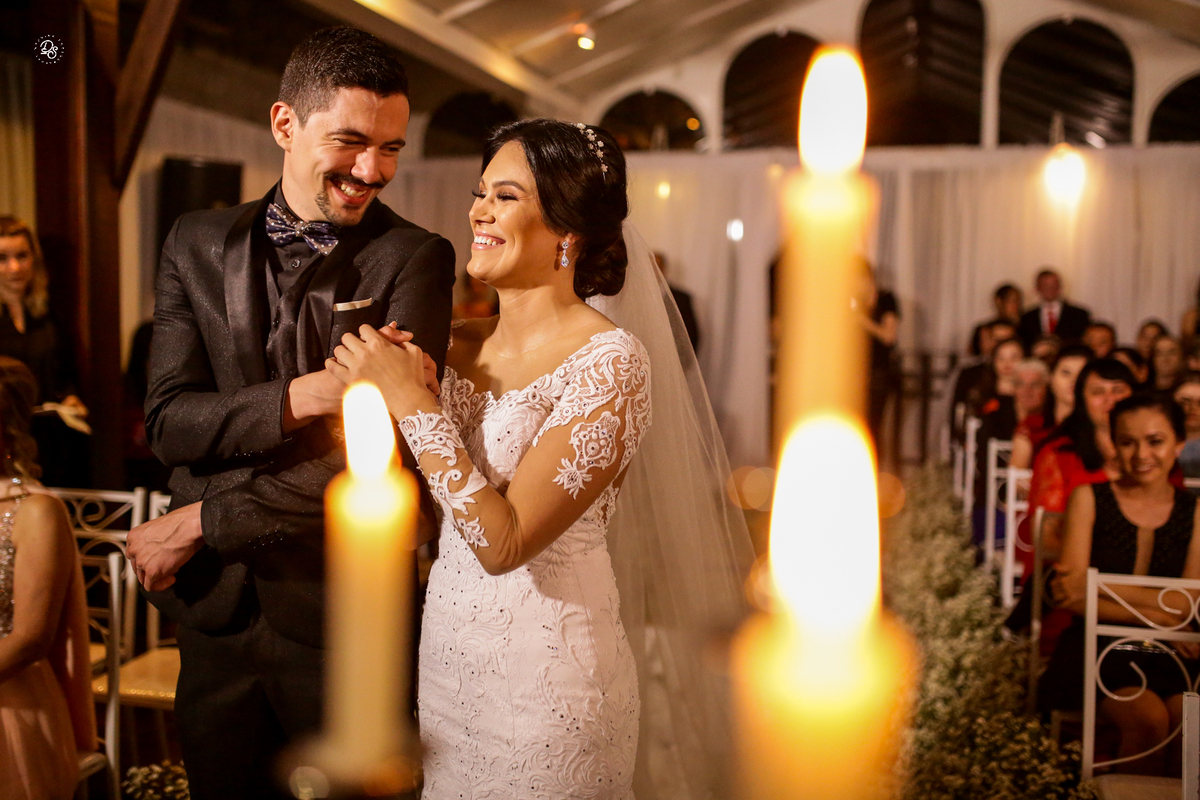 Noivos se olhando e sorrindo com detalhe das velas em desfoque.