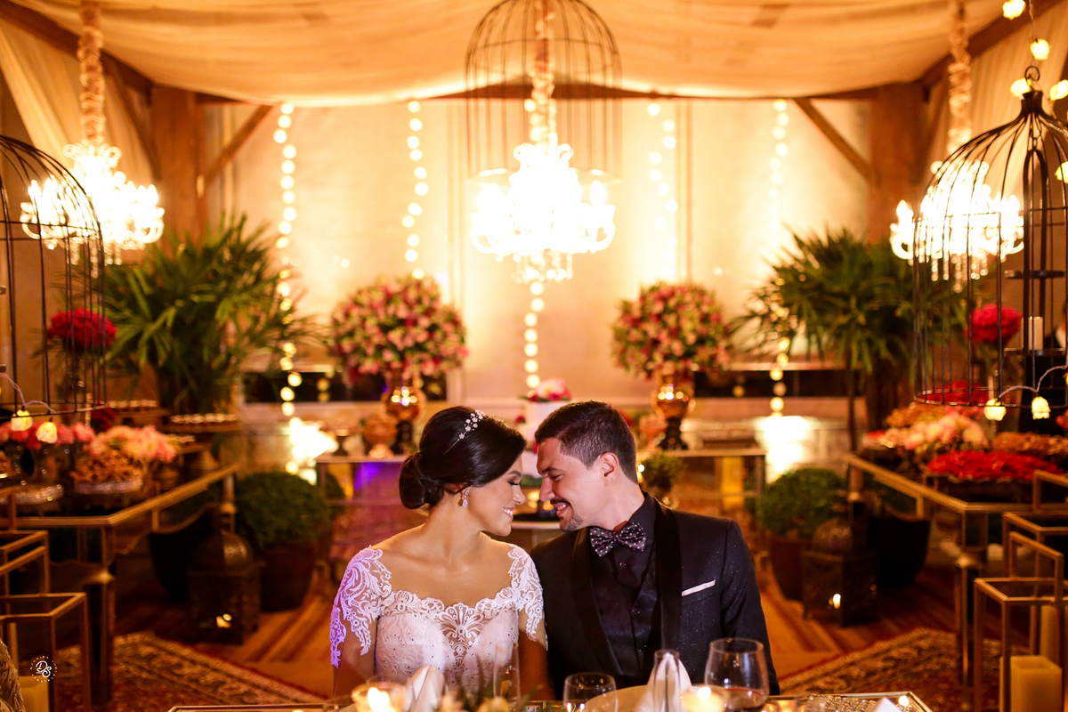 Noivos sentados na mesa com o fundo da decoração.