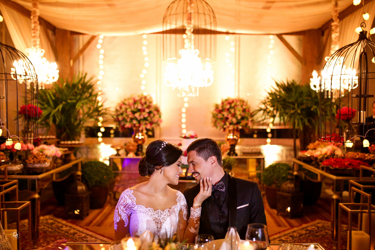 Noivos sentados na mesa com o fundo da decoração.