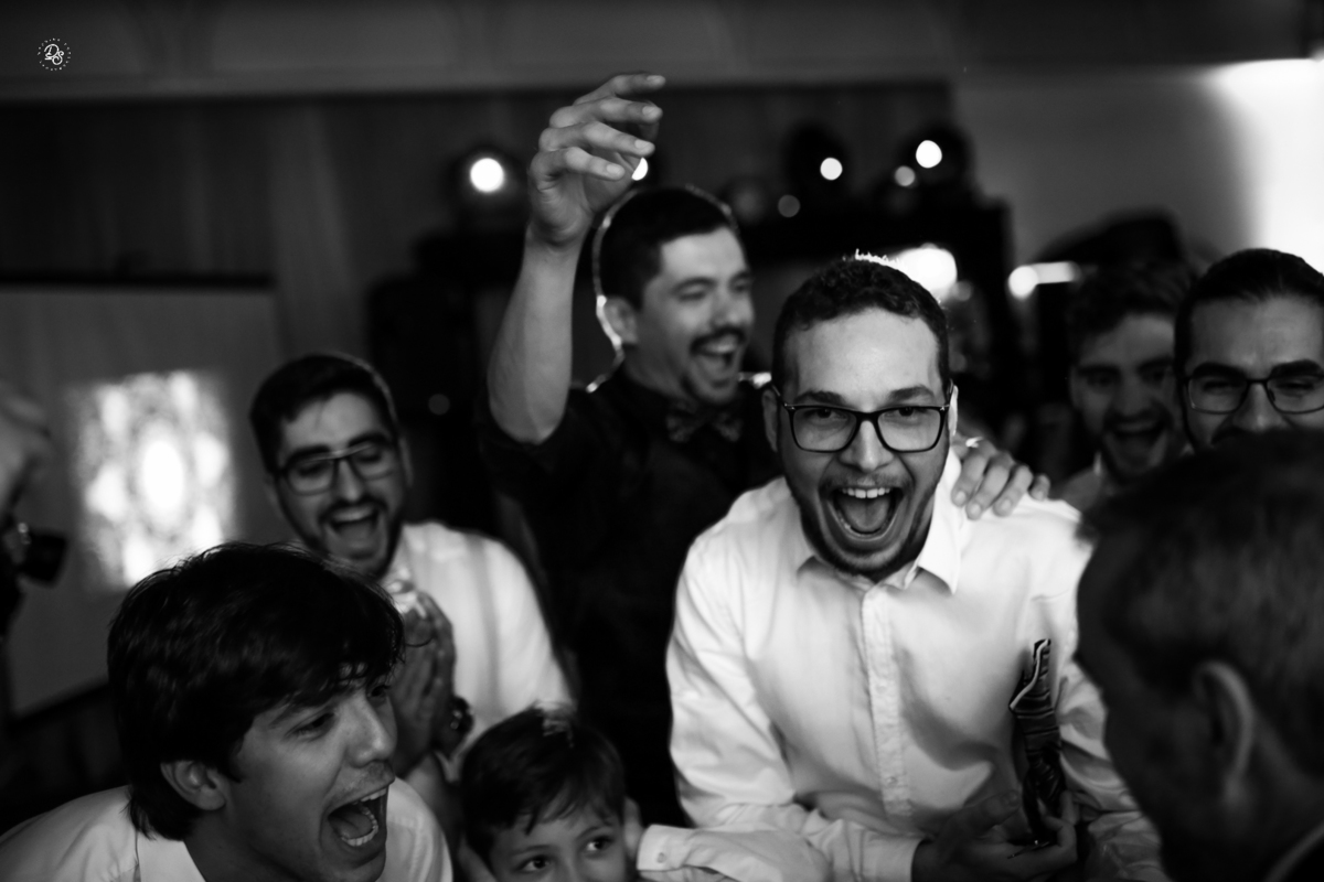 Padrinhos sorrindo e gritando no momento de passar a gravata para os convidados.
