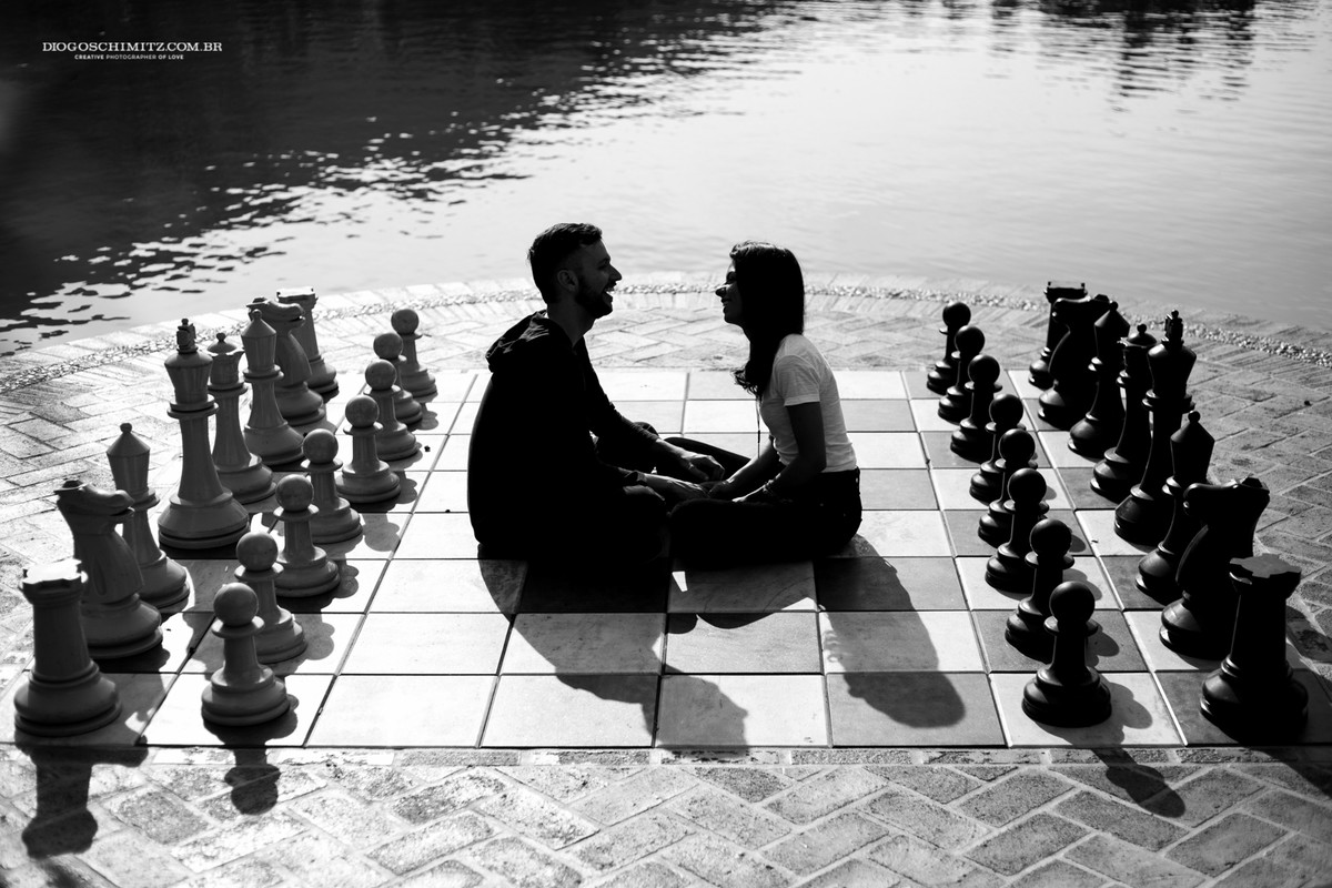 Casal sentado, um de frente para o outro em um tabuleiro de xadrez gigante.