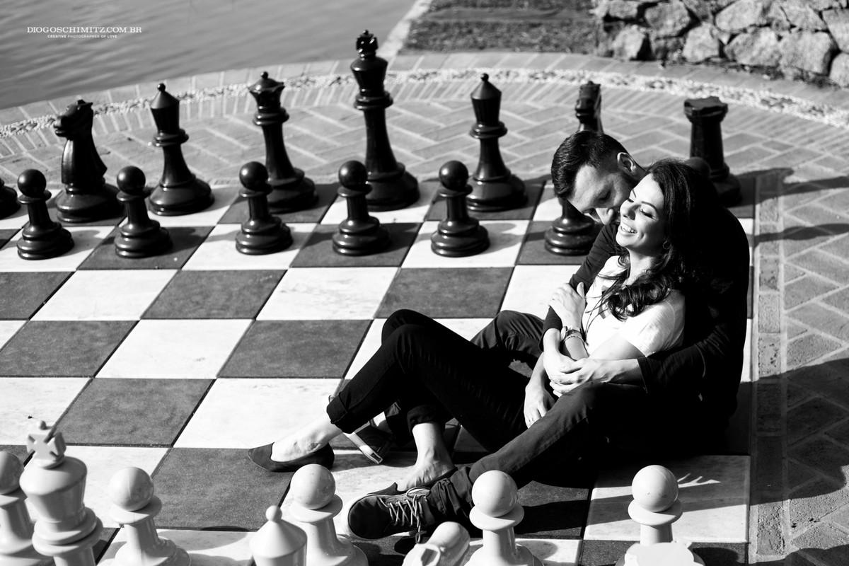 Casal deitado em um tabuleiro de xadrez e rindo.