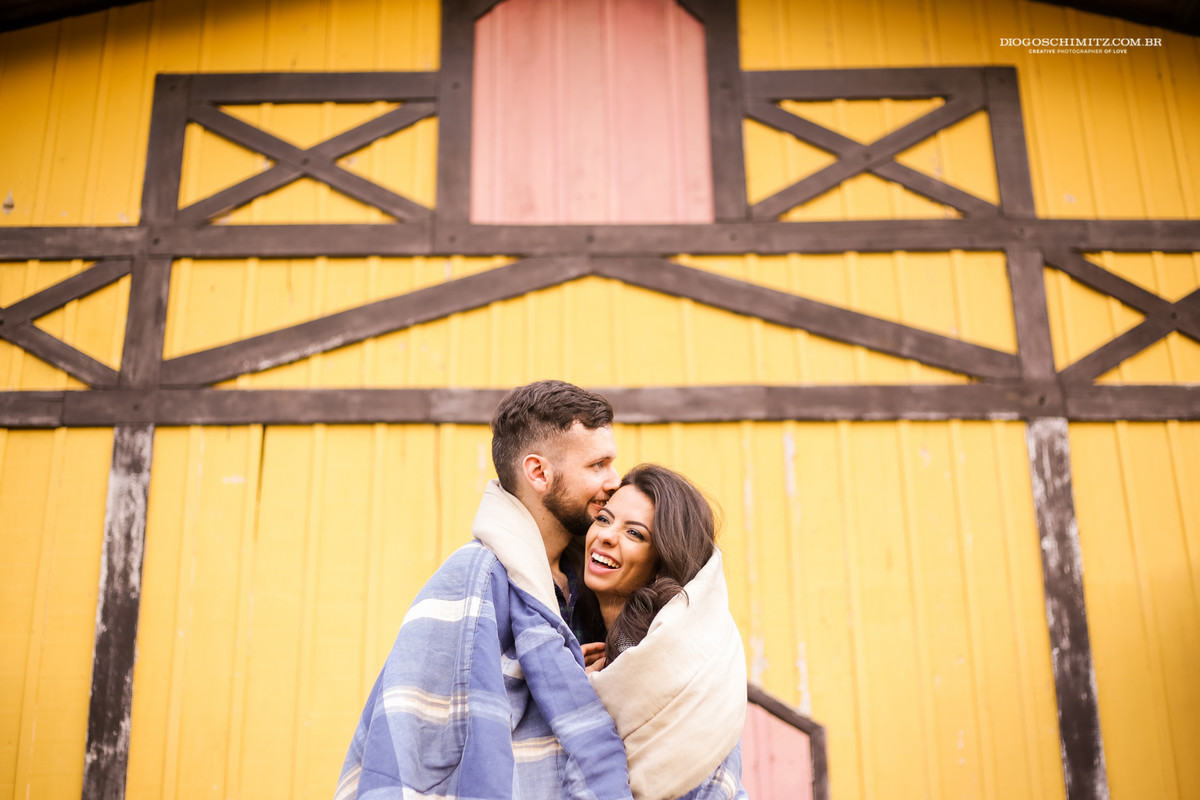 Casal envolto em um edredom sorrindo.