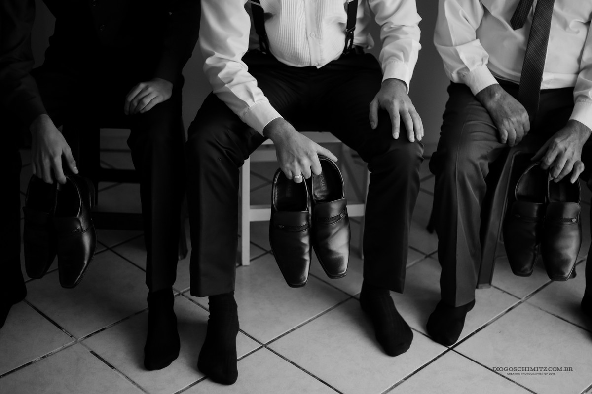 O noivo sentado segurando seus sapatos.