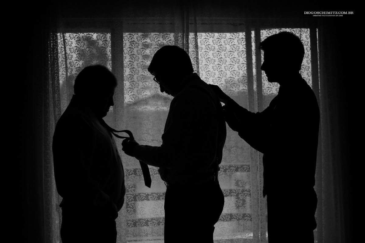 Noivo arrumando a gravata do irmão enquanto seu pai o ajuda a se arrumar.