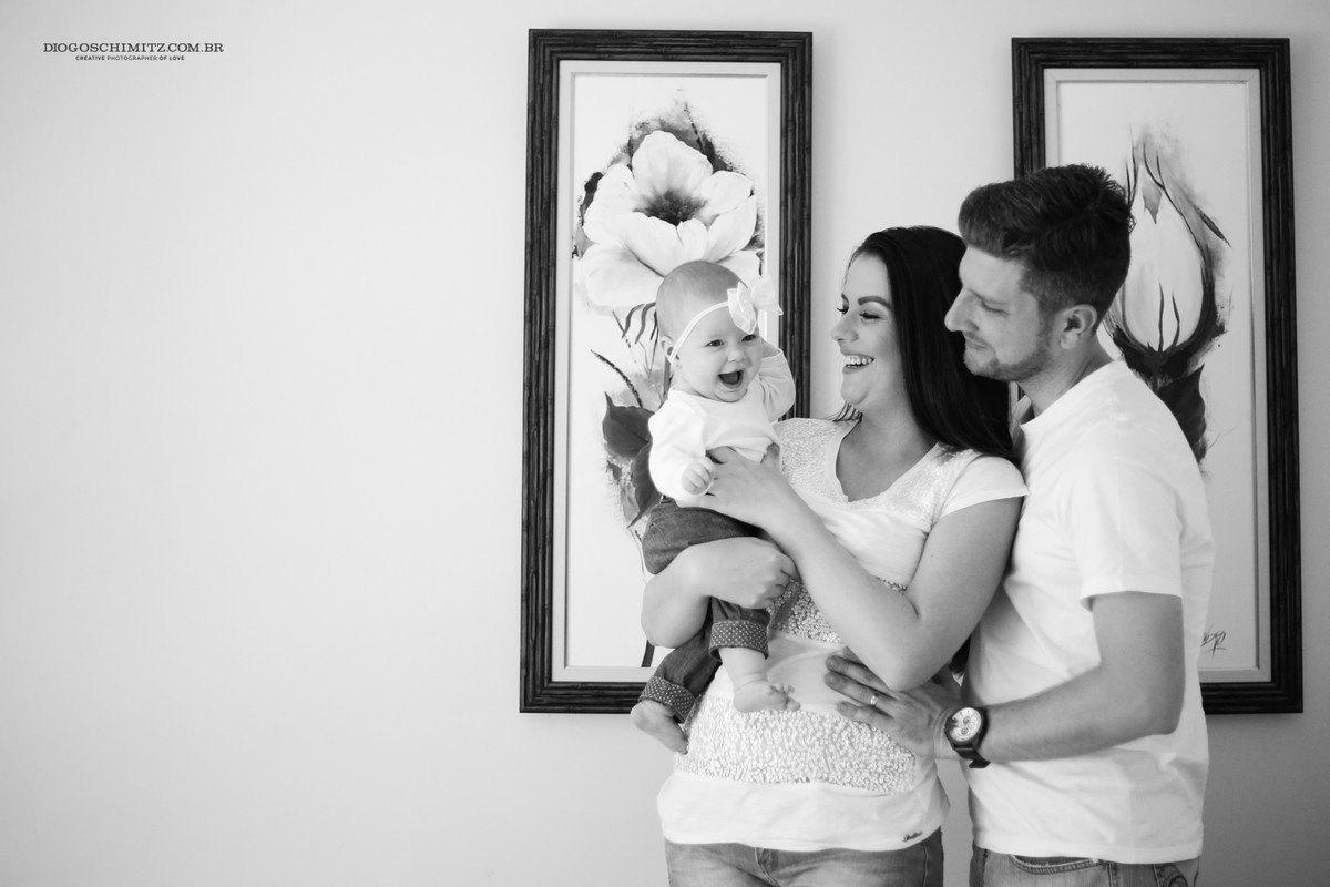 Casal com a filha mais nova em frente a um quadro, a mãe segura a filha enquanto esta sorri.