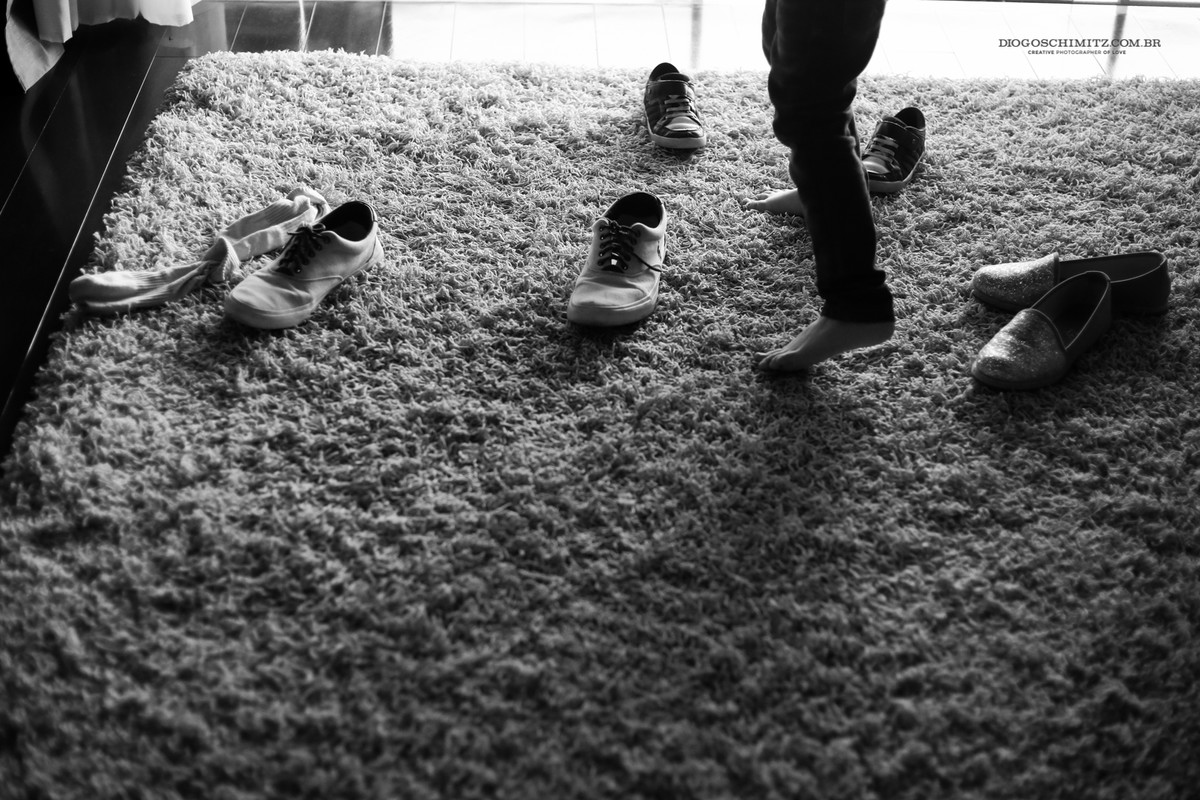 Sapatos em cima de um tapete em frente a uma janela, as pernas do pai aparecem na foto.