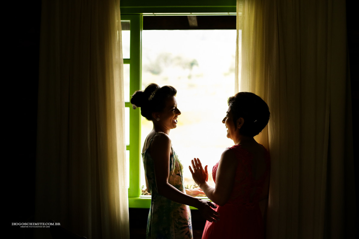 Noiva e sua mãe olhando o noivo pera janel a sorrindo.