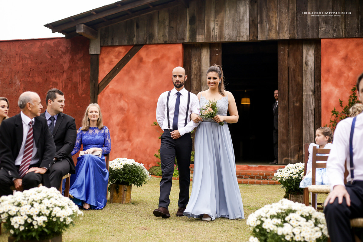 Segundo casal de padrinhos entrando no casamento no campo com vestidos iguais, e buquê na mão.