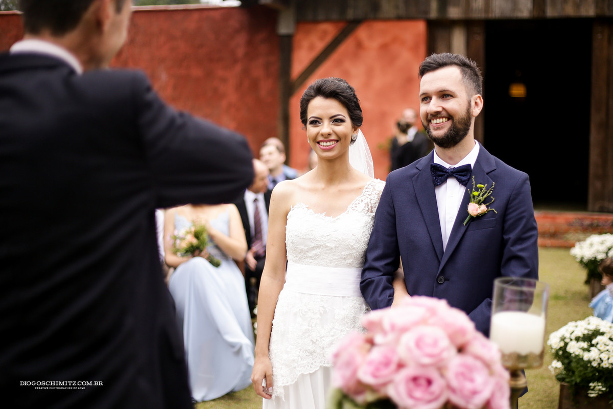 Noivos olham para pastor que comanda a cerimônia do casamento no campo.