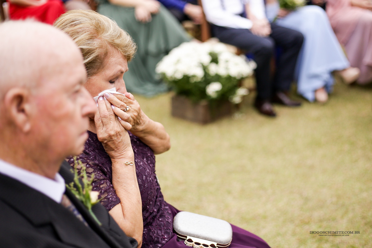 Mãe do noivo chora e limpa as lágrimas com um lenço.