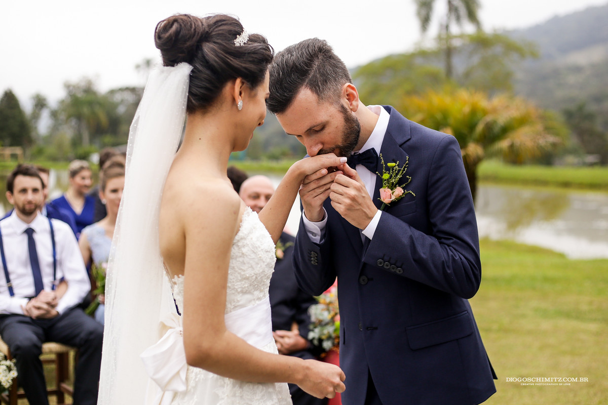 Noivo beija a mão da noiva ao colocar a aliança de casamento.