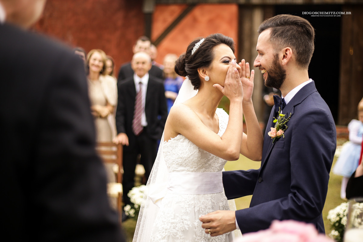 Noiva tenta esconder o momento do beijo, noivo sorri.