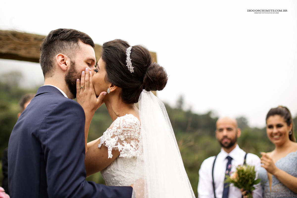 Foto do momento do beijo em que noiva esconde o beijo com as mãos.