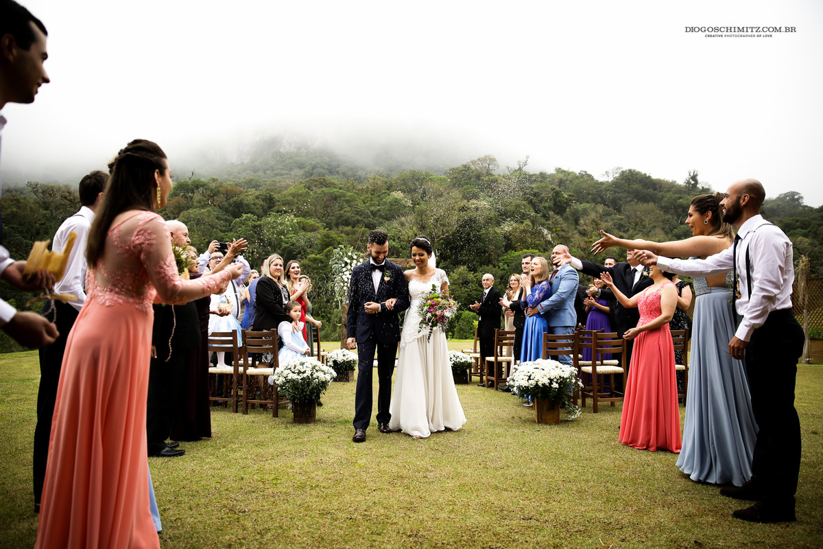 Noivos sorrindo ao receber a chuva de arroz na saída da cerimônia no campo.