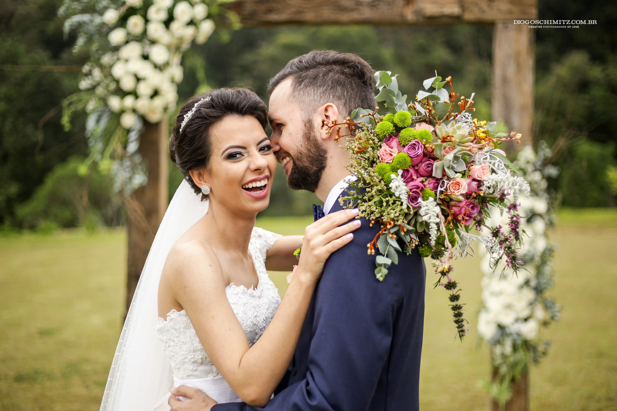Noiva sorri para o noivo, buquê de casamento no campo.