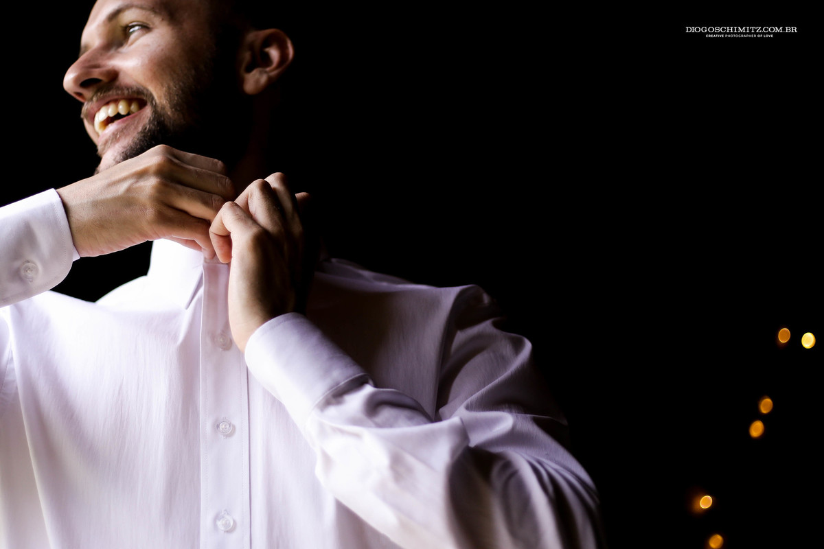Noivo arrumando sua camisa para casamento de dia no campo.