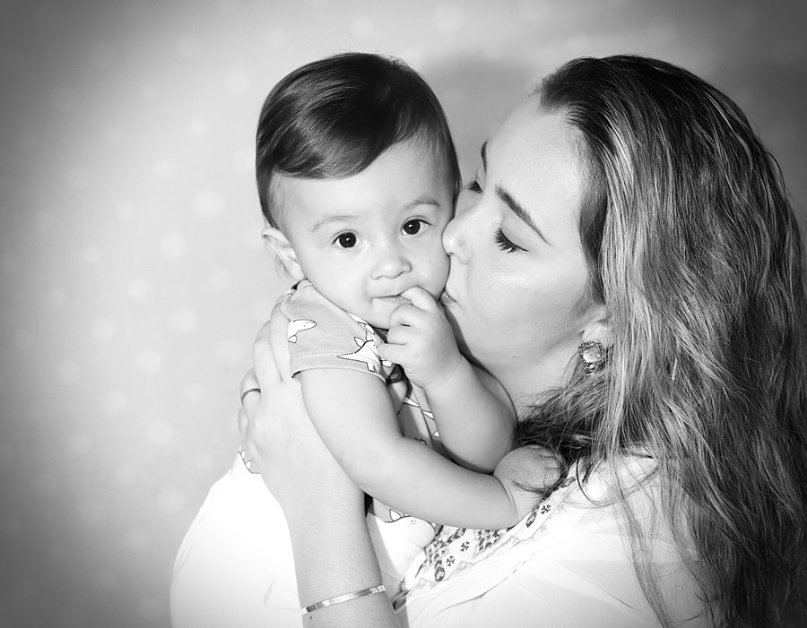 Fotografia em preto e branco do bebê no colo da mãe recebendo um beijo-Rio de Janeiro-RJ