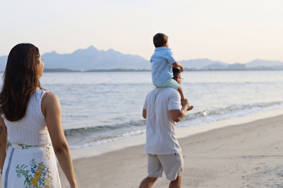 Fotografia dos pais com o filho caminhando em  uma praia- Rio de Janeiro - RJ