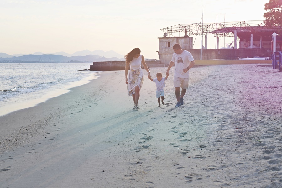 Fotografia dos pais com o filho caminhando em  uma praia- Rio de Janeiro - RJ