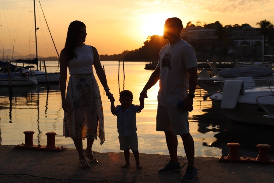 Fotografia dos pais com o filho no pôr do sol em um deck - Rio de Janeiro - RJ
