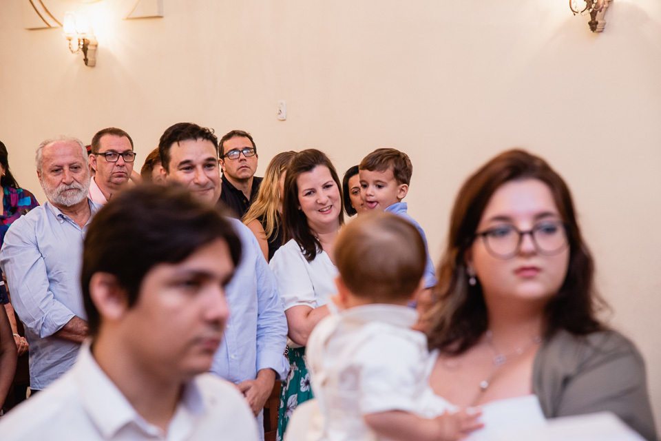 durante o batizado do benjamin olhando e sorrindo para os pais