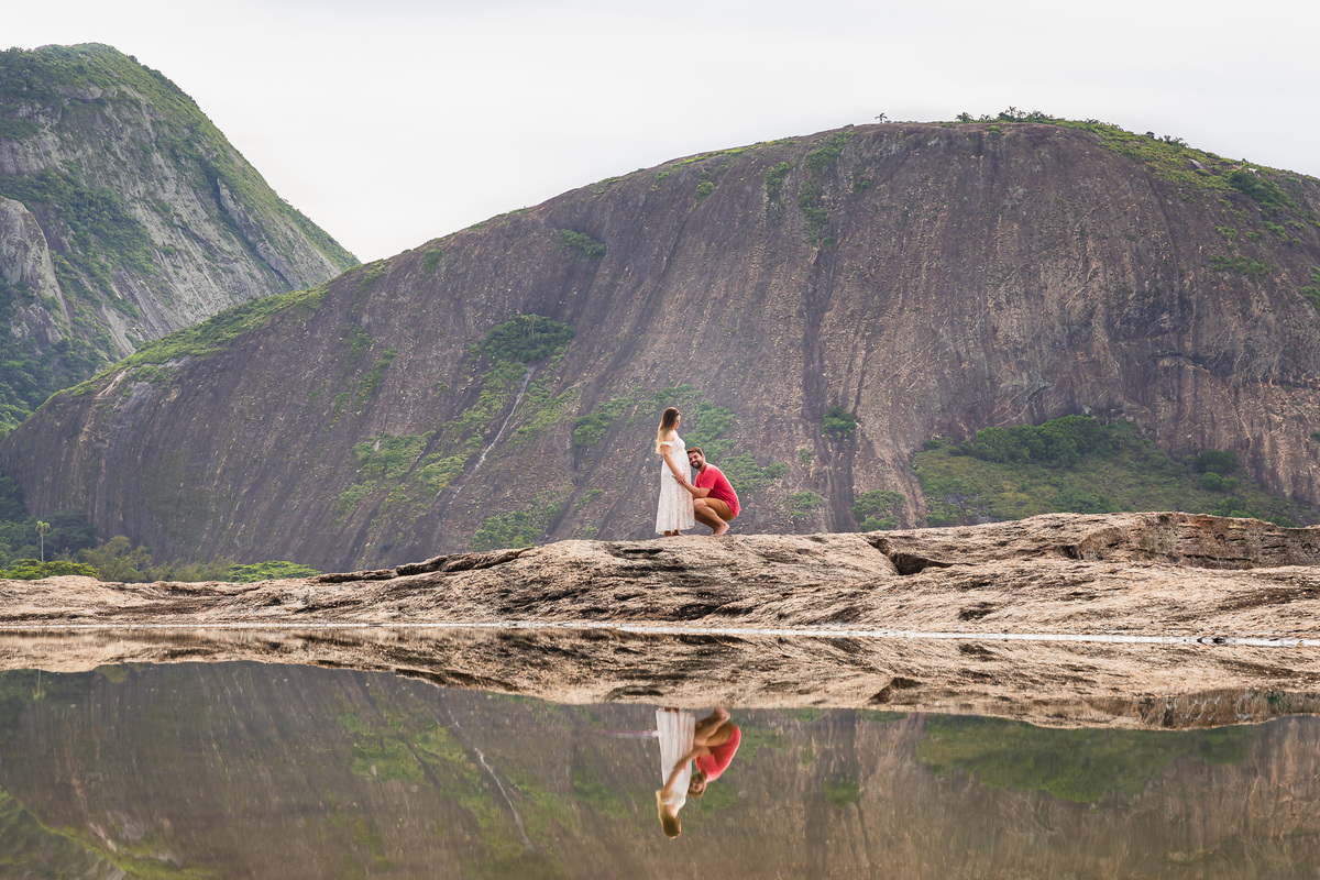 casal gestante de mãos dadas com a imagem refletida na água da pedra do pampo em itacoatiara niteroi rj