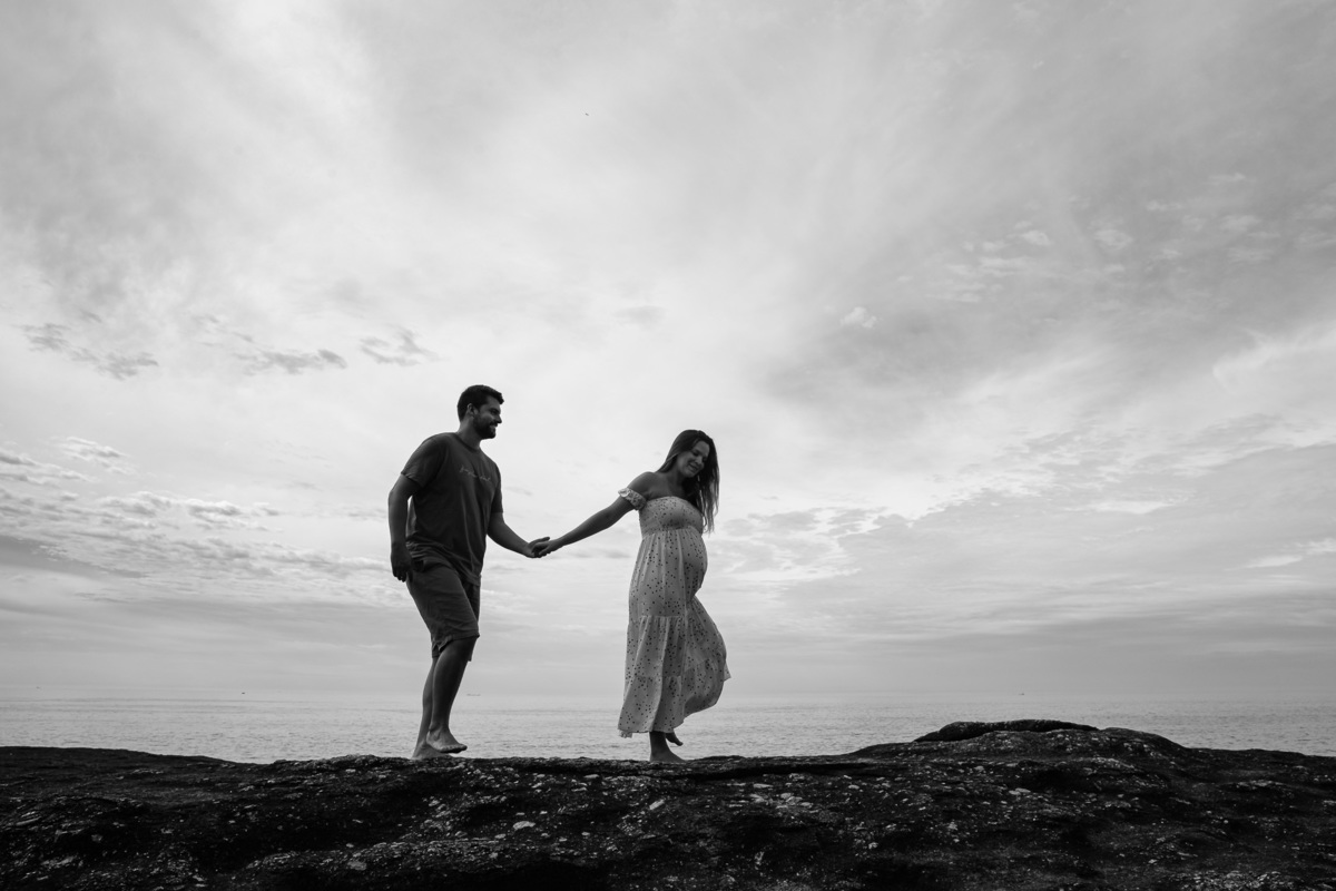 casal gestante de mãos dadas andando na pedra do pampo em itacoatiara niteroi rj