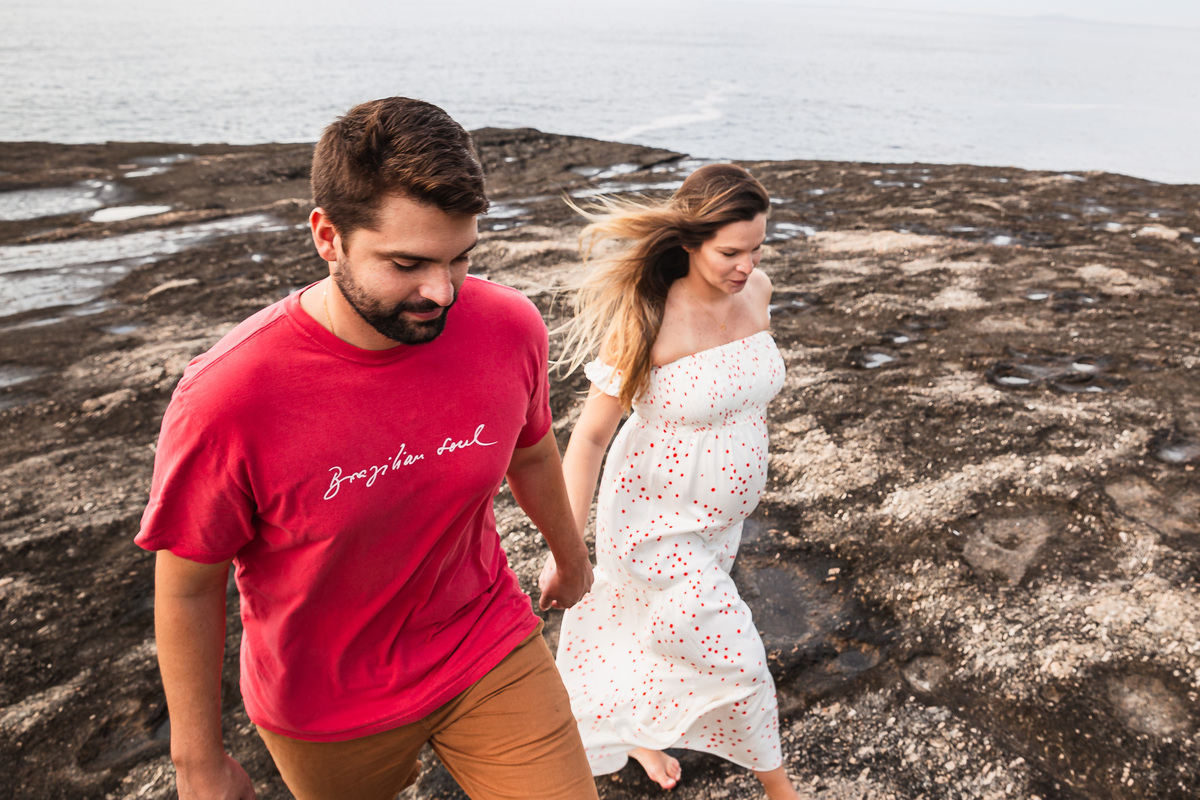 casal gestante de mãos dadas andando na pedra do pampo em itacoatiara niteroi rj