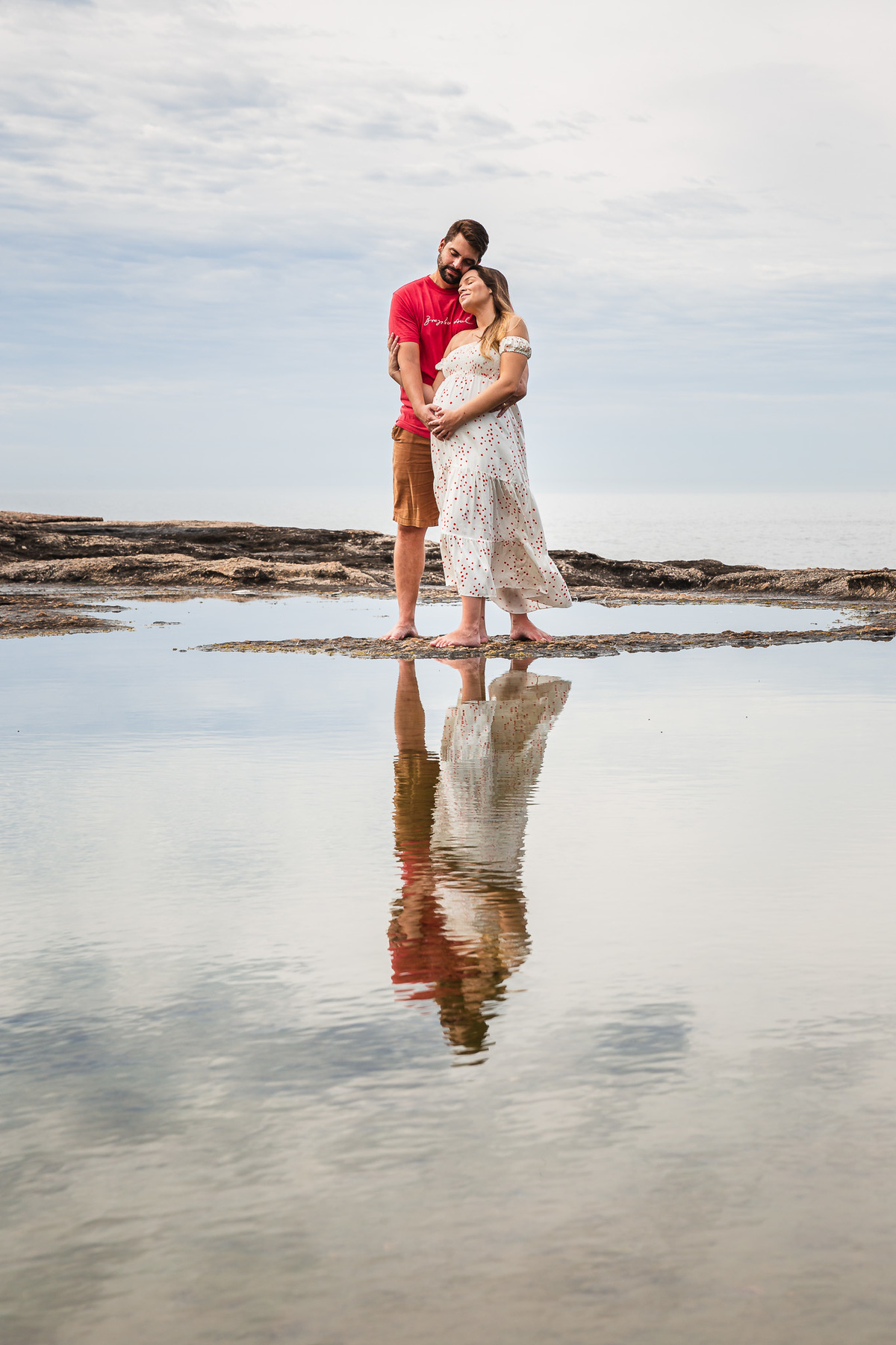 casal gestante de mãos dadas com a imagem refletida na água da pedra do pampo em itacoatiara niteroi rj