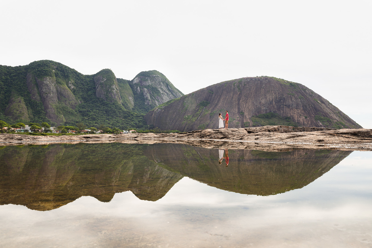 casal gestante de mãos dadas com a imagem refletida na água da pedra do pampo em itacoatiara niteroi rj