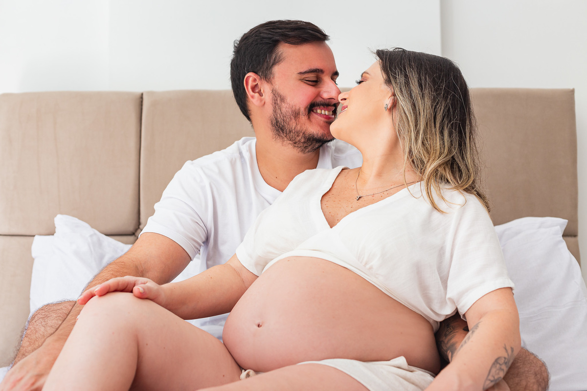 casal com 30 semanas de gestação posando pra foto se beijando em cima da cama de casal