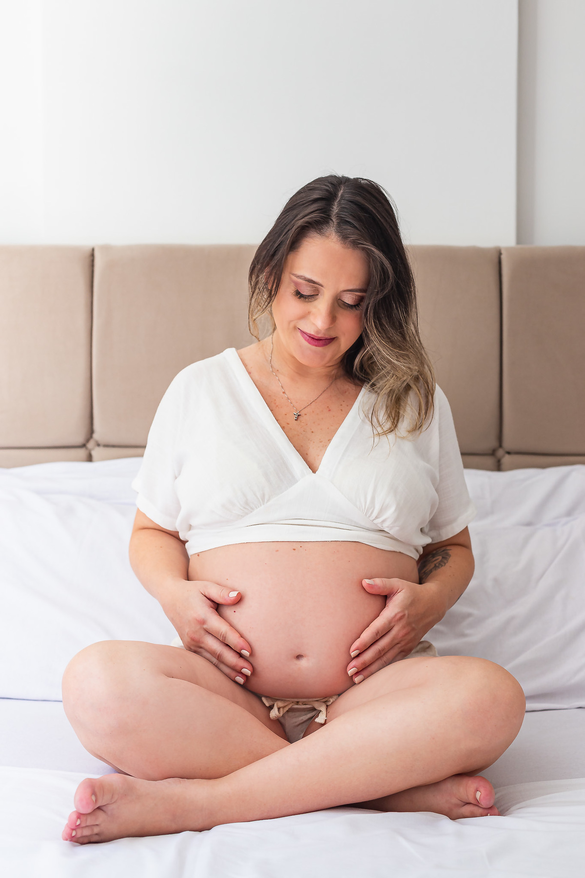 mãe com 30 semanas de gestação posando pra foto com a mão na barriga em cima da cama de casal