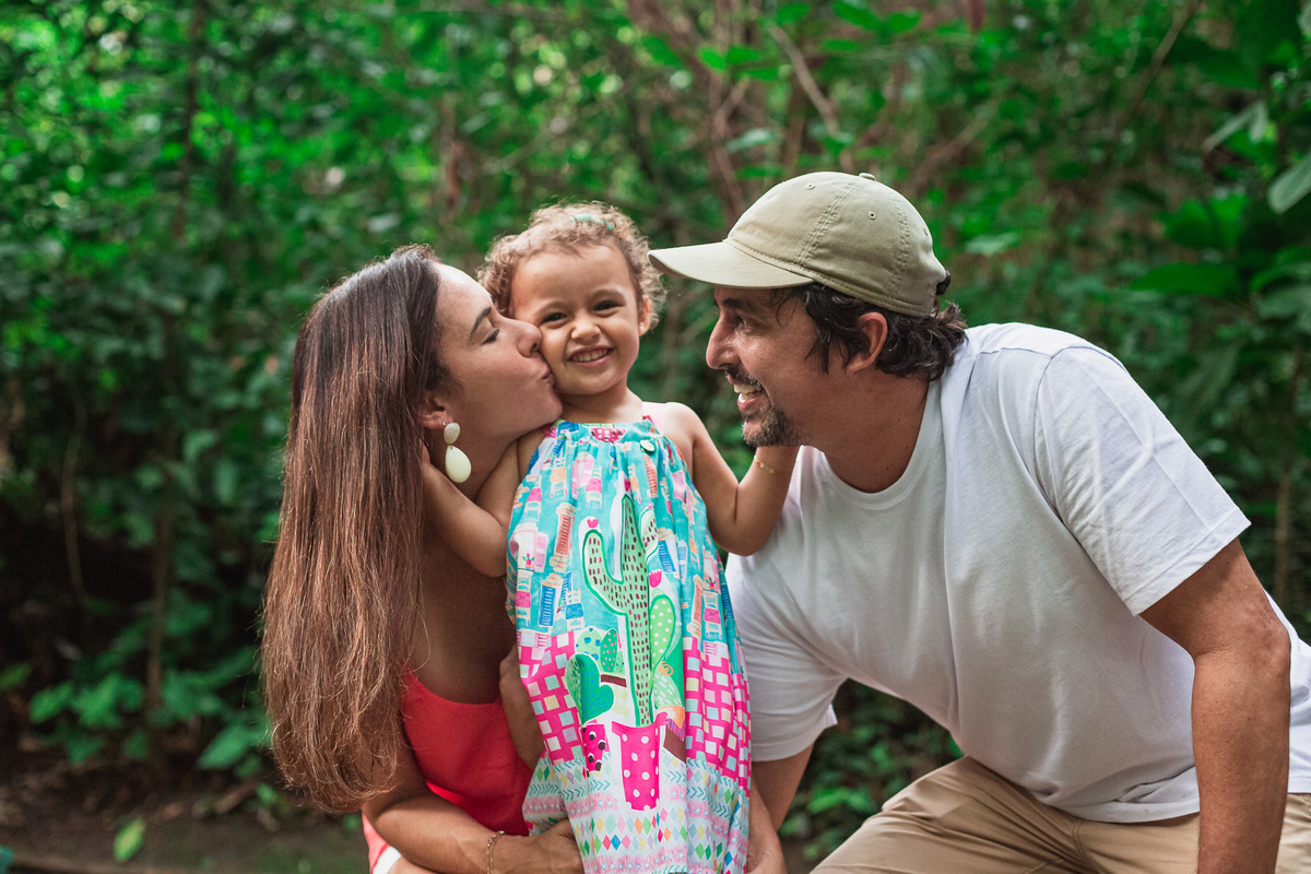 ensaio fotografico em familia no parque da catacumba filha abraçando pai e mae dando beijo