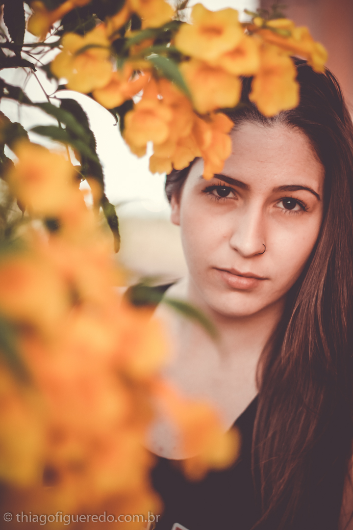 entre as flores a bela Bruna olha para as lentes do fotógrafo de ensaio fotográfico de jaú e região Thiago Figueredo em local cheio de cores