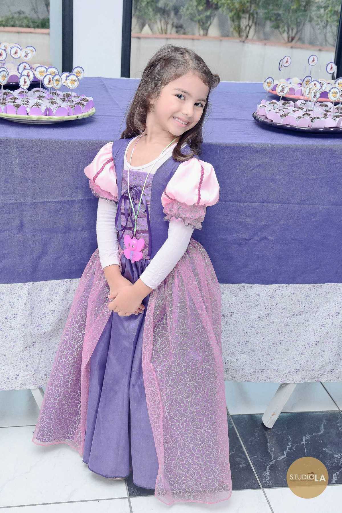 Uma linda menina fantasiada de princesa posa sorridente em frente à mesa decorada, durante sua festa infantil. Fotografia de festa infantil em São Paulo feita pelo Studio LA.