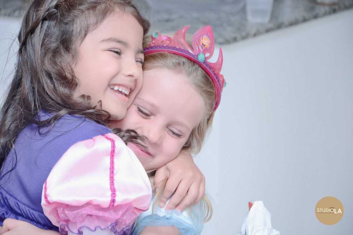 Amigas se abraçam com carinho e sorrisos em uma festa infantil encantadora. Registro espontâneo e cheio de ternura feito pelo Studio LA.