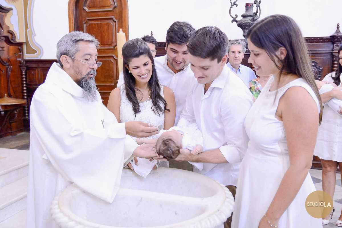 Batizado católico em São Paulo: momento da pia batismal com a família reunida e o padre realizando o sacramento. Registro de batizado feito pelo Studio LA.