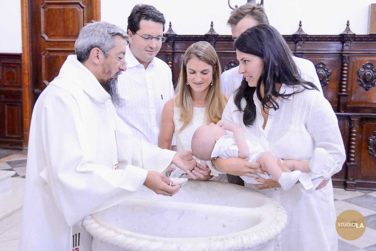 Família reunida ao redor da pia batismal durante a cerimônia de batizado católico em São Paulo. Uma fotografia que transmite união e espiritualidade, captada pelo Studio LA.