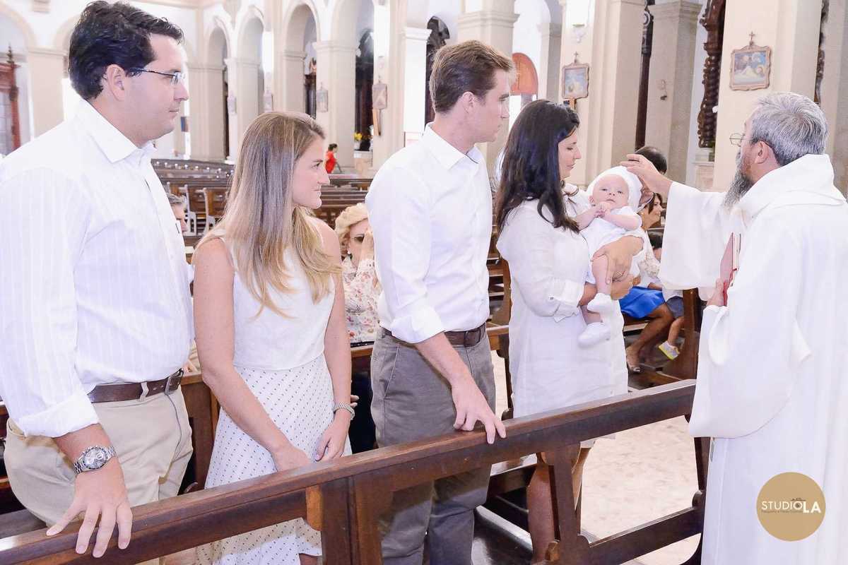 Momentos de fé: mãe com bebê no colo recebendo a bênção do padre durante o batizado católico. Registro cheio de significado feito pelo Studio LA em São Paulo.