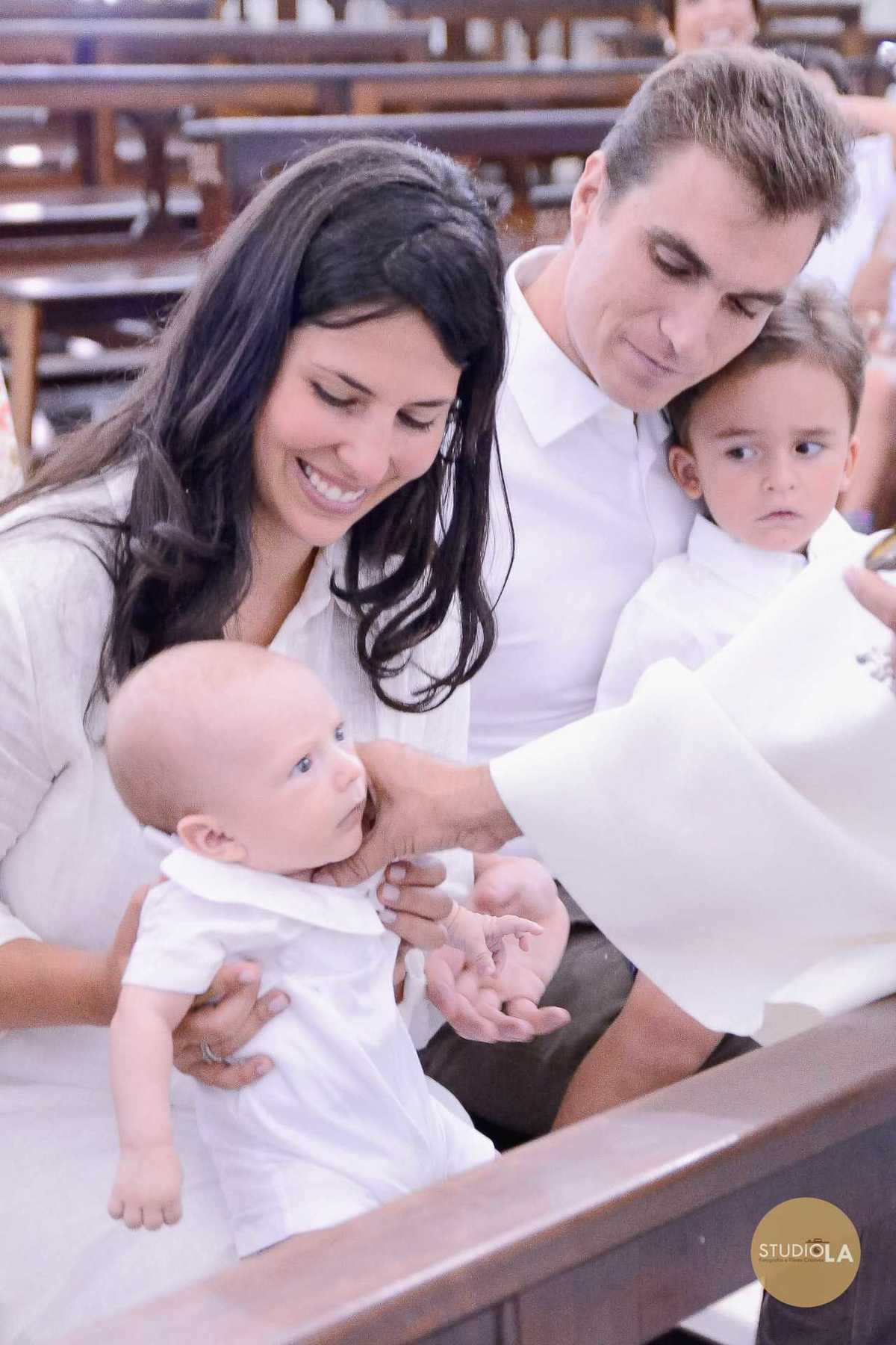 Detalhe emocionante do batizado: bebê no colo da mãe recebendo a bênção do sacerdote. Fotografia delicada de batizado feita pelo Studio LA na igreja católica em São Paulo.