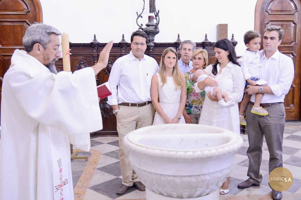 Sacramento do batismo: bênção do padre diante da pia batismal com a família reunida. Fotografia de batizado feita pelo Studio LA em São Paulo.