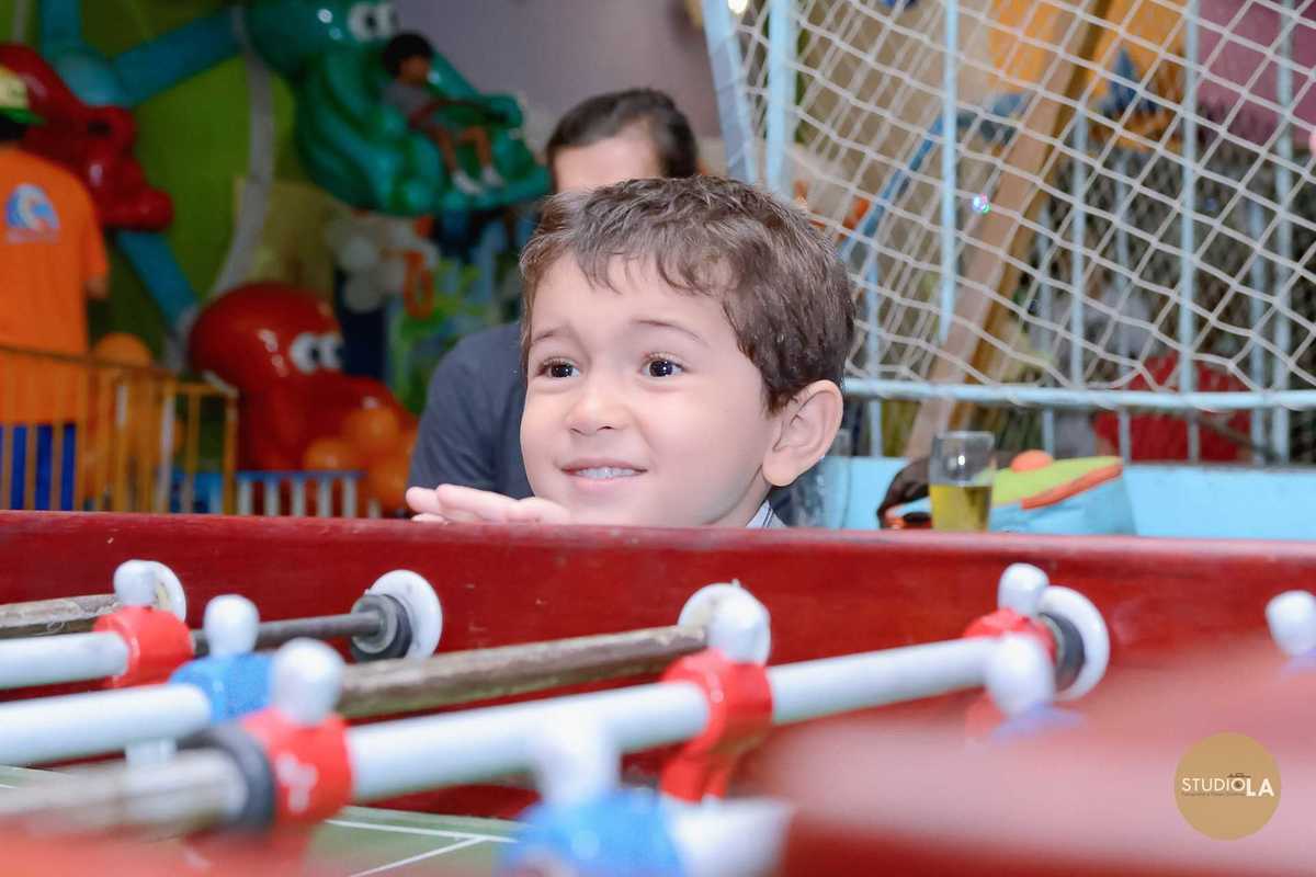 Criança observando a partida de pebolim com olhar encantado durante o aniversário infantil no buffet, registrando um momento espontâneo — fotografias de festa infantil feitas pelo Studio LA.