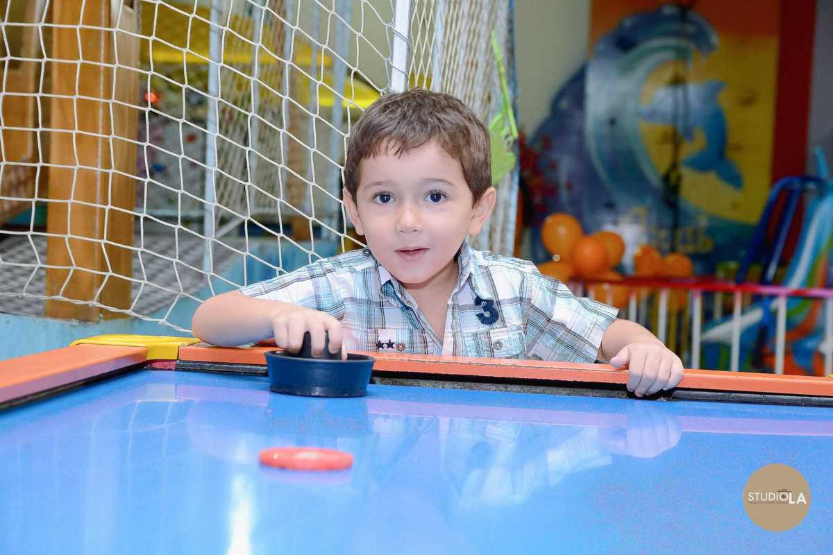 Menino se divertindo na mesa de air hockey durante a festa infantil no Buffet Azul do Mar em SP. Registro de alegria feito pelo Studio LA.
